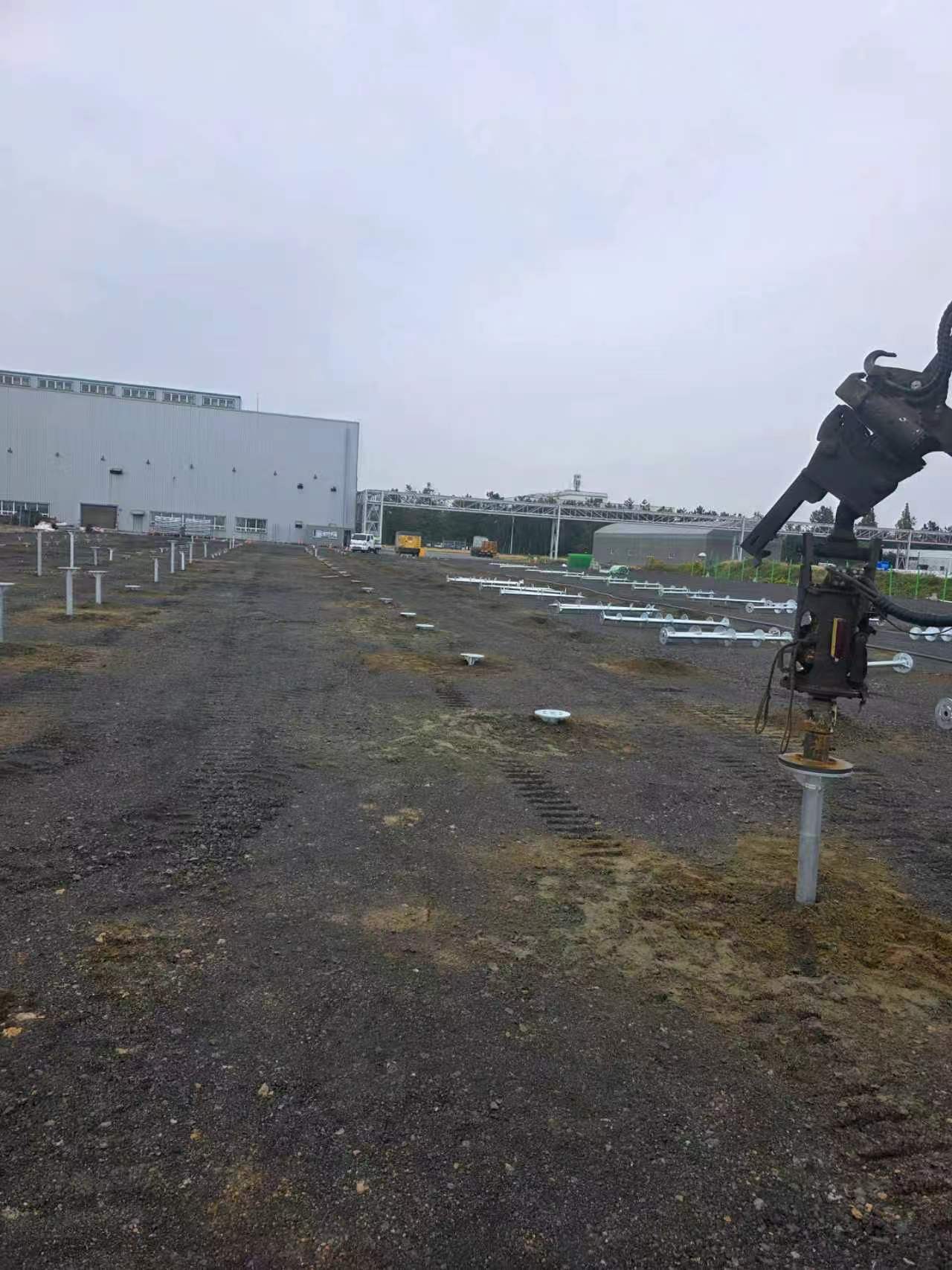 Excavator-mounted pile driver installing a spiral ground screw on a solar project site